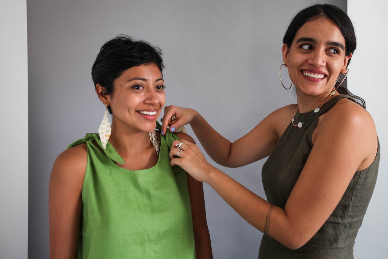 Two women smiling as they style and adjust earrings indoors.